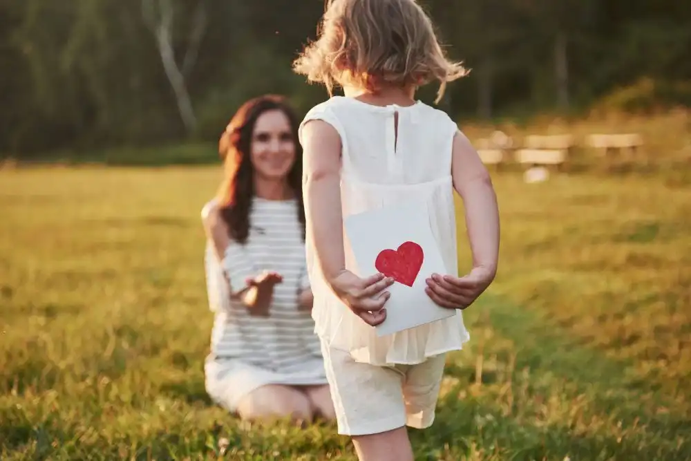 Figlia piccola che cammina verso la madre con un disegno come regalo in un prato